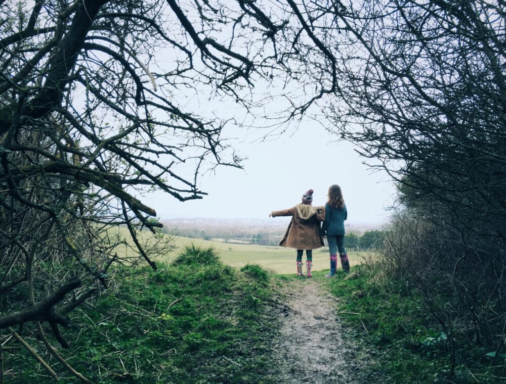 Path through trees leading to an opening with two young girls in winter clothing looking for the way forward.