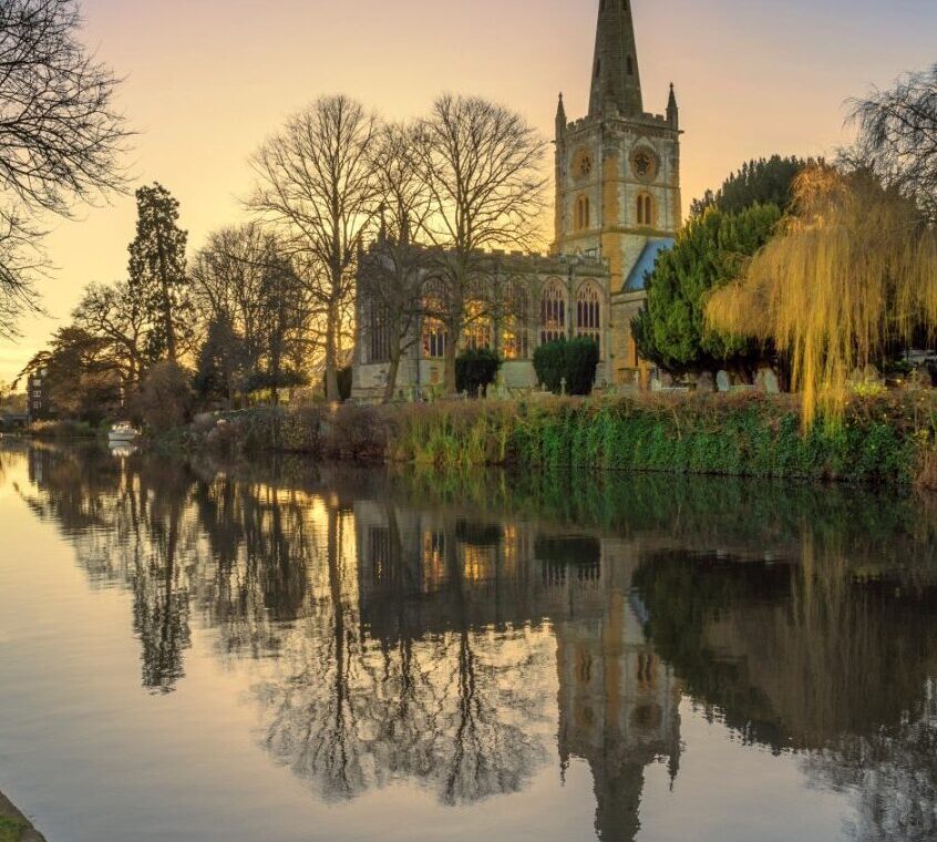 A church sits on a river, in Stratford Upon Avon at dusk.